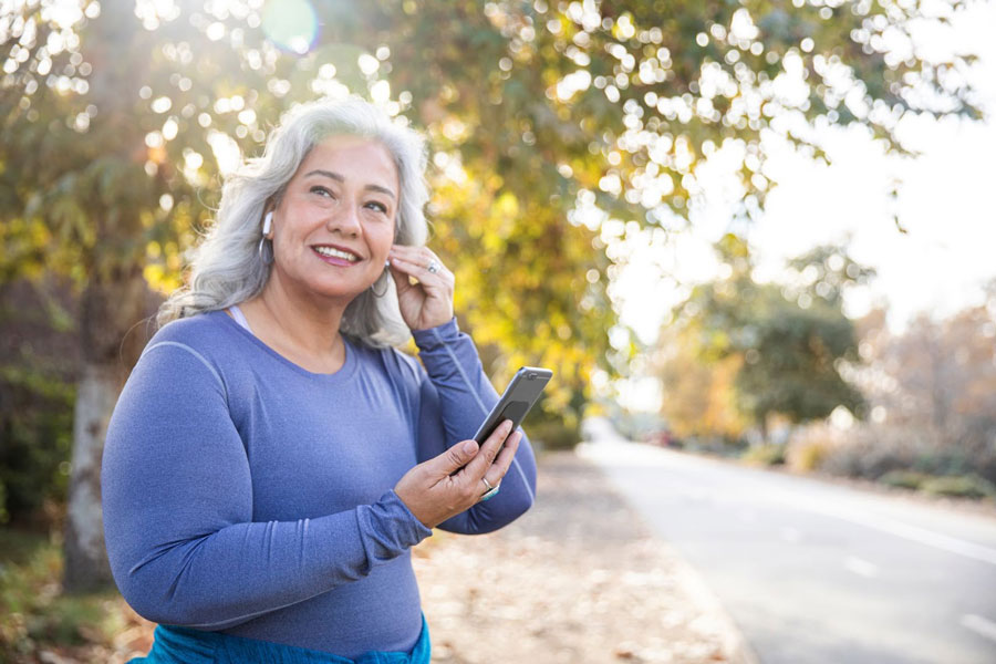 c0a2f184-blog_hero_best_podcasts senior woman outside in workout gear, putting in wireless headphones