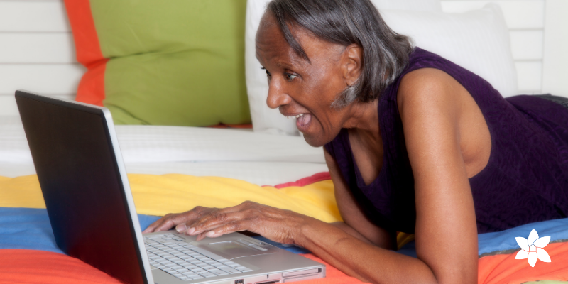 Senior woman laying down, smiling at a laptop screen