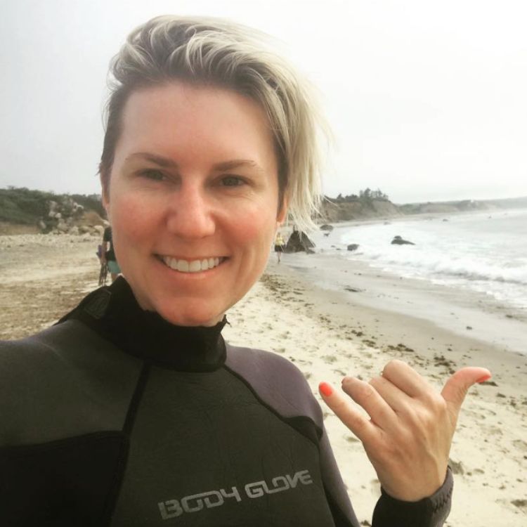 Sevy Petras on a beach in surfing wetsuit.
